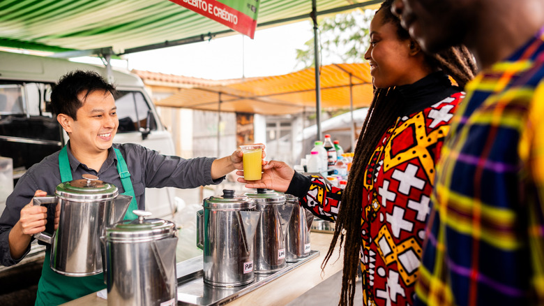 food vendor giving woman a glass of sugarcane juice