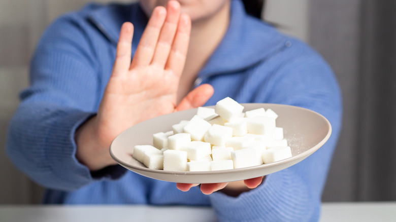 woman pushing away plate with pile of sugar cubes