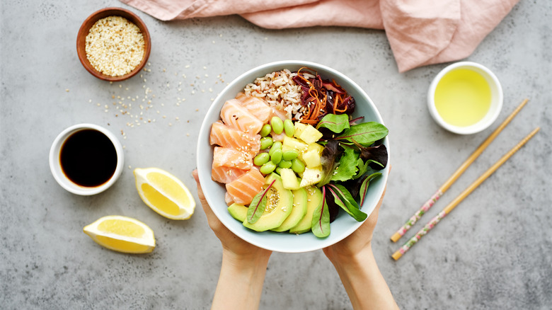 A woman holds a poke bowl with edamame in it