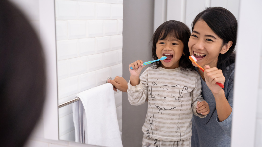 mom and daughter brushing their teeth while looking in the mirror 