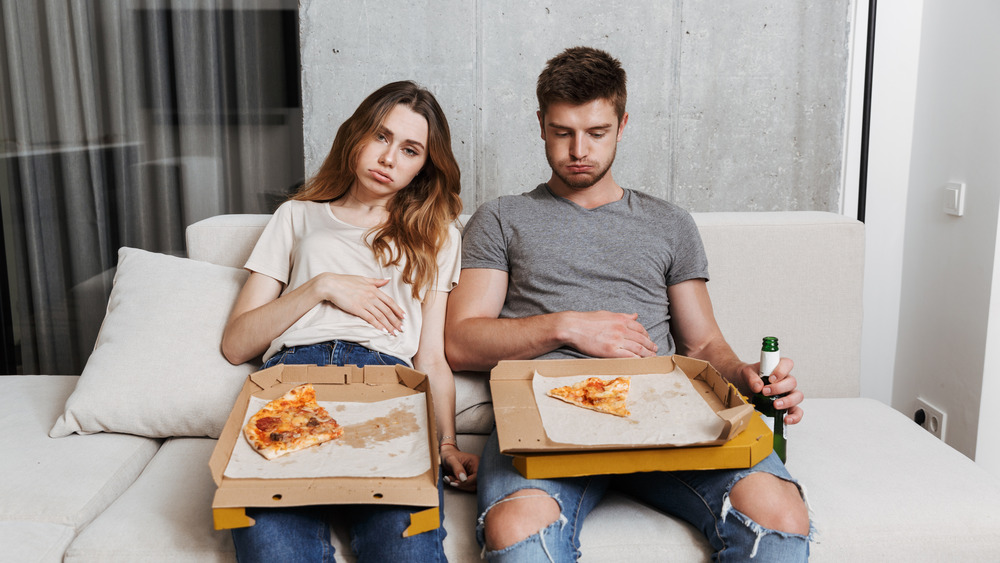 Unhappy couple with pizza and stomach pain sitting on their couch 