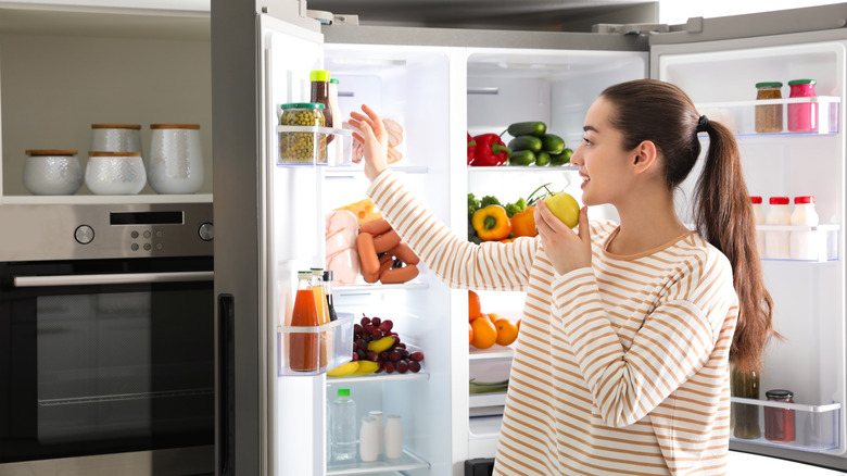 A woman eats an apple near the fridge