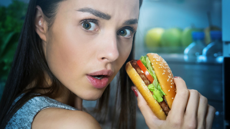 a woman eating in front of the fridge at night