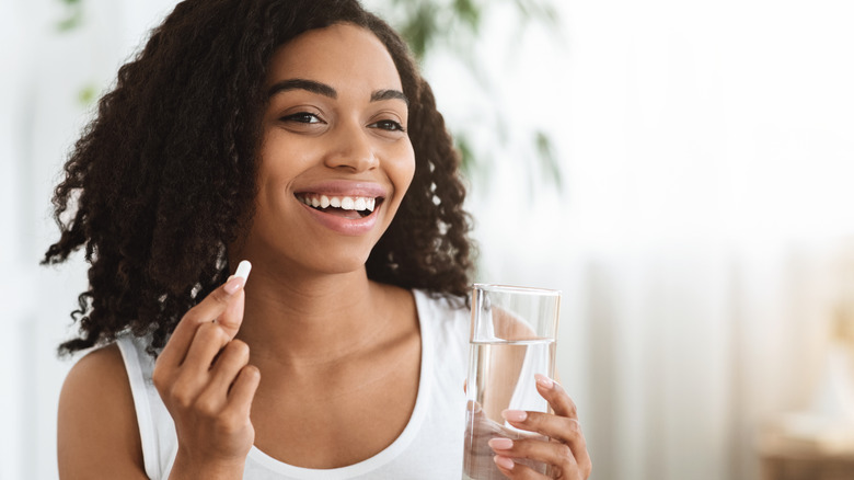 Woman takes vitamin with glass of water. 