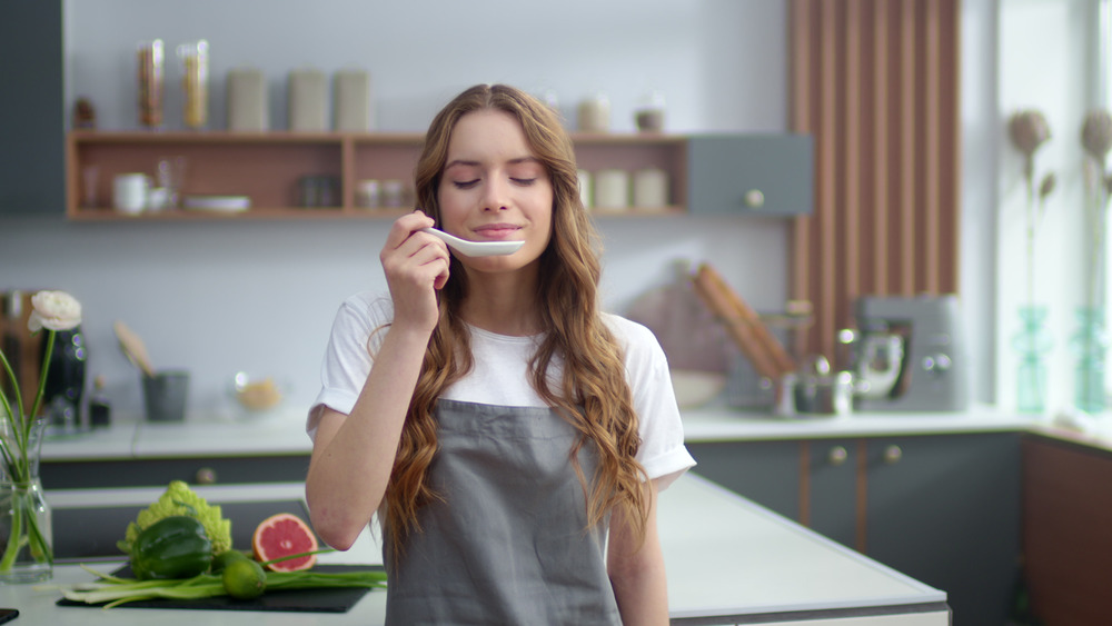 Young woman smelling spoon in kitchen