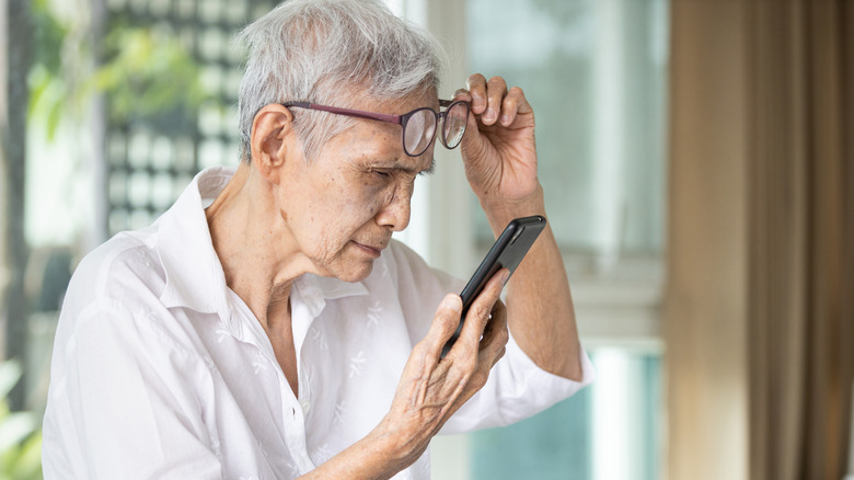 Senior citizen lifting up glasses and squinting while trying to see something on her cellphone