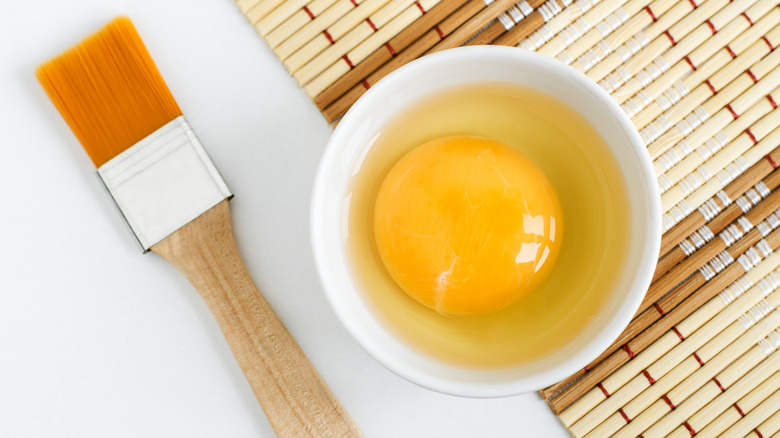 Raw egg in the white bowl next to cosmetic brush