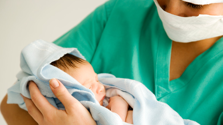 Doctor wearing scrubs holding newborn baby