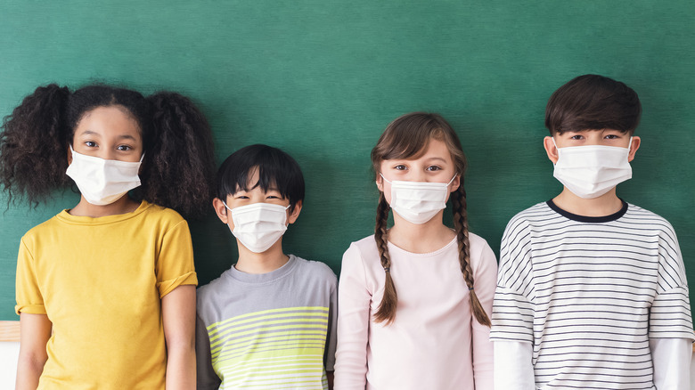 children in masks standing against a chalkboard