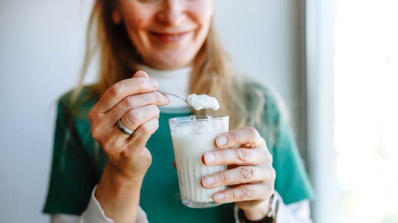 woman holding a spoon of plain yogurt from a glass