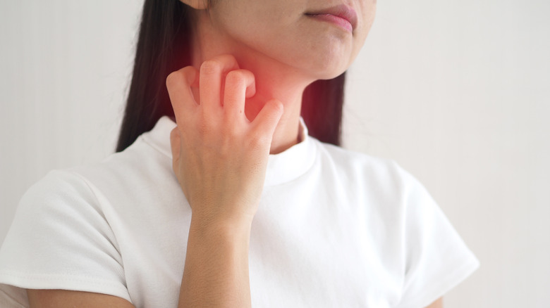 woman in white tee scratching red throat