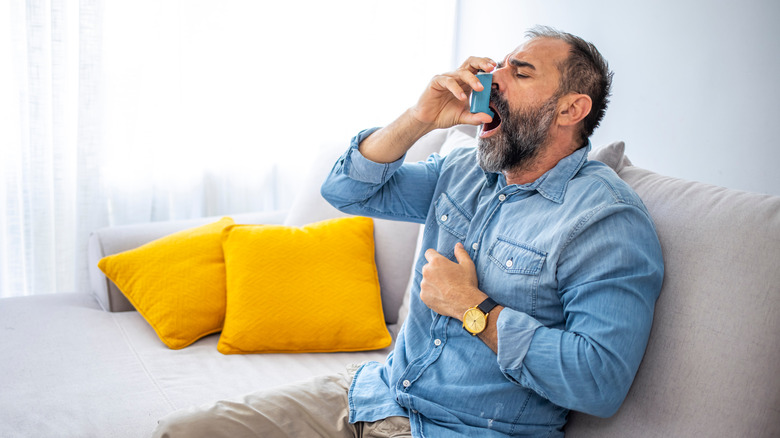 man holding chest and using inhaler on the couch