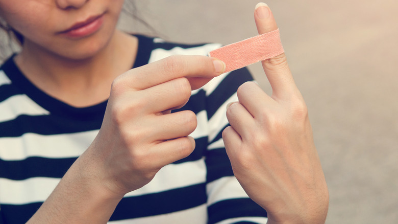 Woman in a striped shirt putting a bandage on the first finger of her left hand