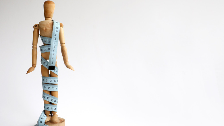 measuring tape wrapped around wooden mannequin