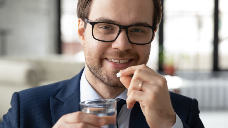 smiling man in suit taking pill