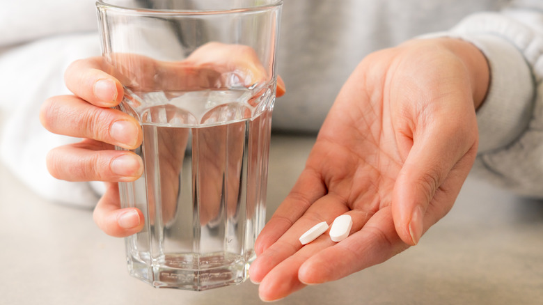 Hand holding pills and water glass