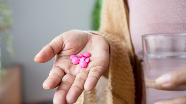 A woman's hand holding several ibuprofen tablets in her palm