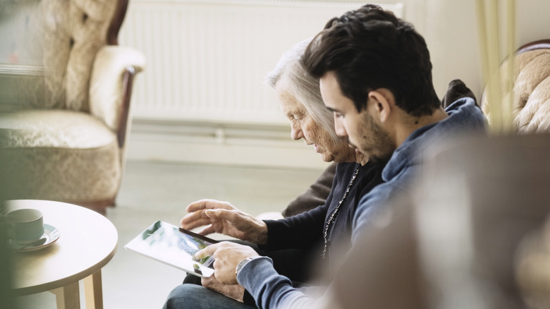 A younger man sitting with an older woman looking at a picture