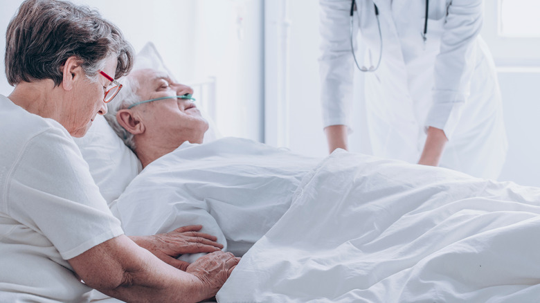 Woman touching arm of man in hospital bed