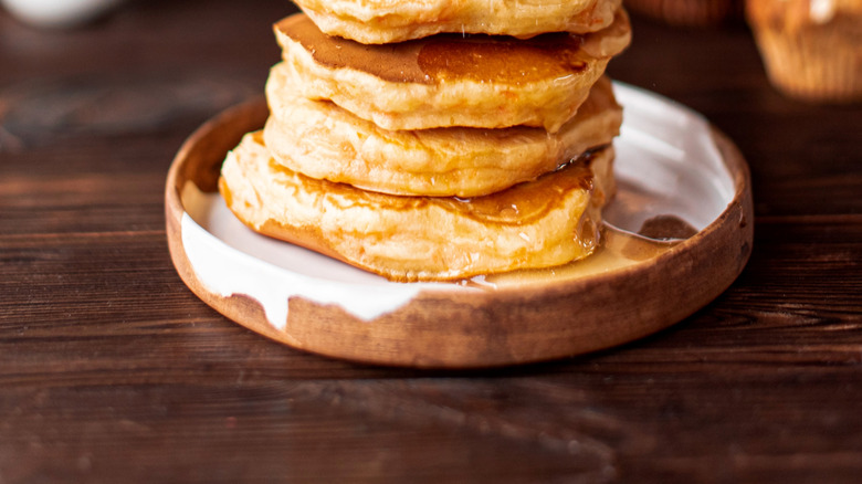 Fluffy pancake stack with powdered sugar and blurred muffins in the back