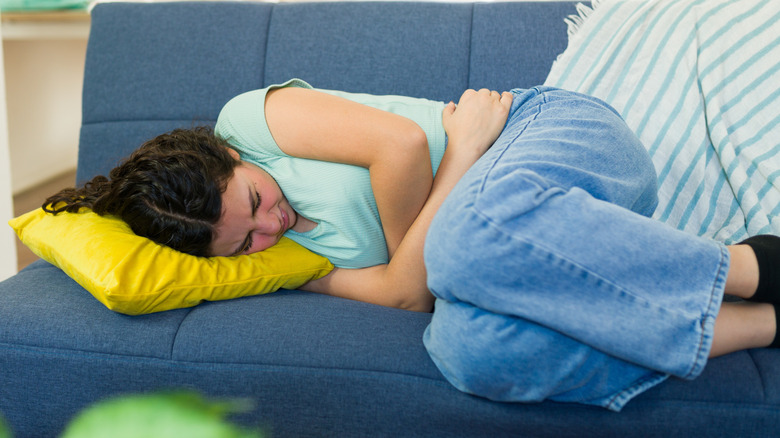 Woman clutching her stomach lying on the couch
