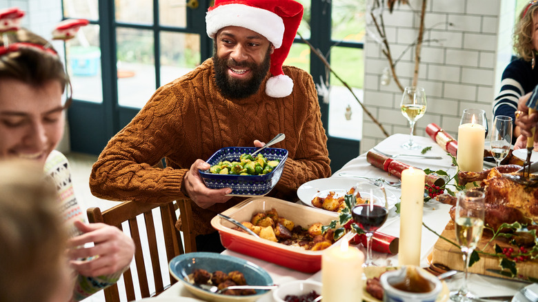 A man at a Christmas party passing Brussels sprouts at the table