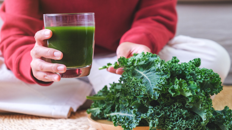A person with a kale smoothie and kale leaves on the table