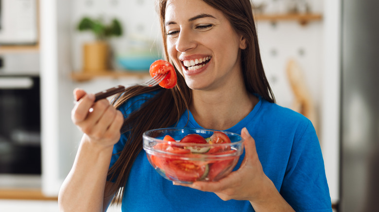 A smiling woman eating tomatoes from a bowl
