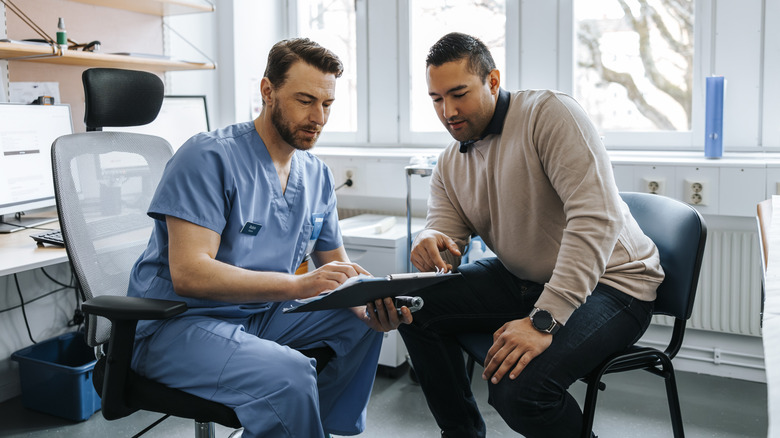 A man and a doctor looking at the doctor's clipboard in the doctor's office