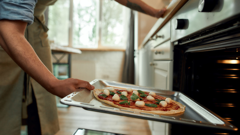 person putting pizza into oven