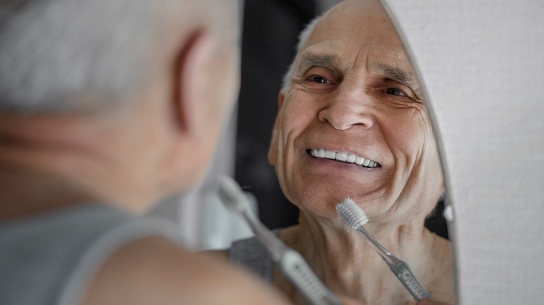 Older man brushing teeth in mirror