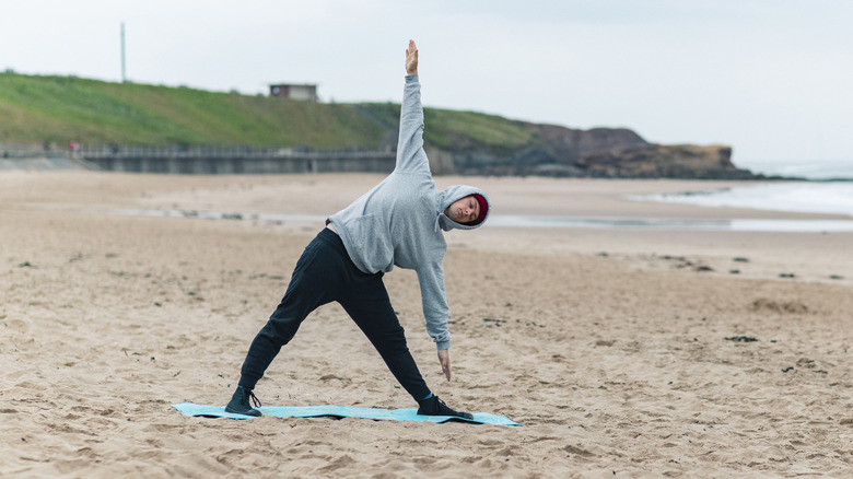 man doing triangle yoga pose on a beach