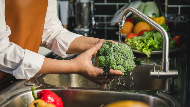 woman washes broccoli at her kitchen sink