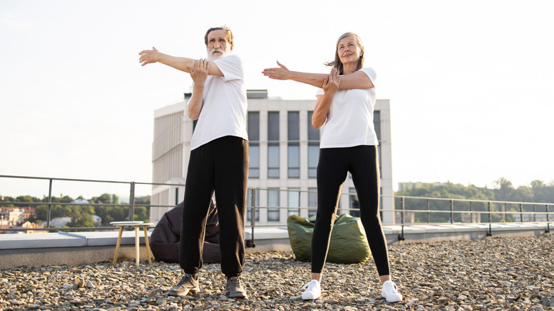 An older man and woman stretching their arms while outside