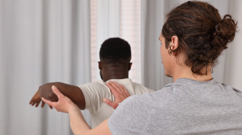 Physical therapist adjusting man's shoulder