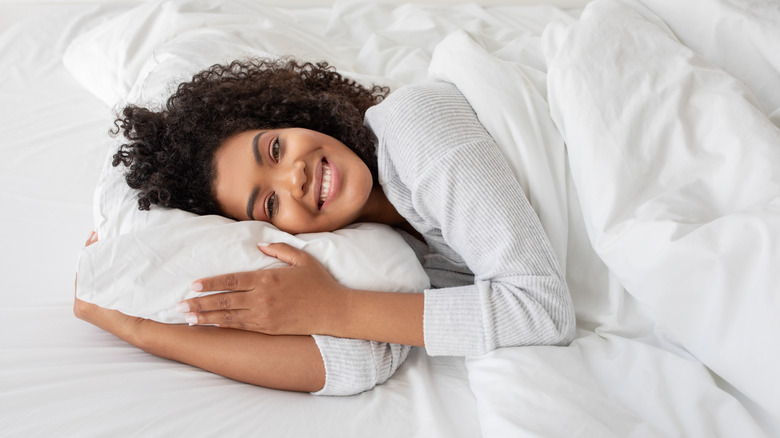 A woman smiling while lying in a white bed