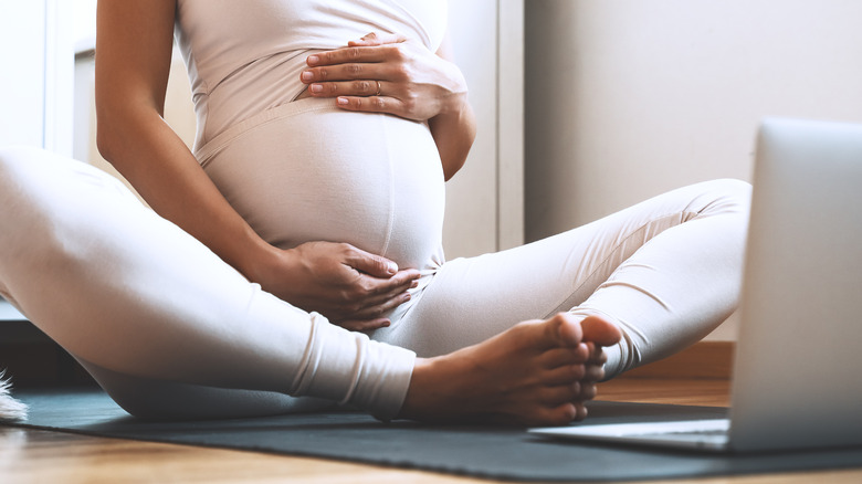 pregnant woman on mat watching laptop