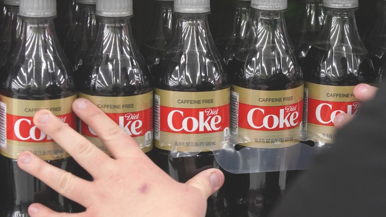 hand touches diet coke bottles on shelf