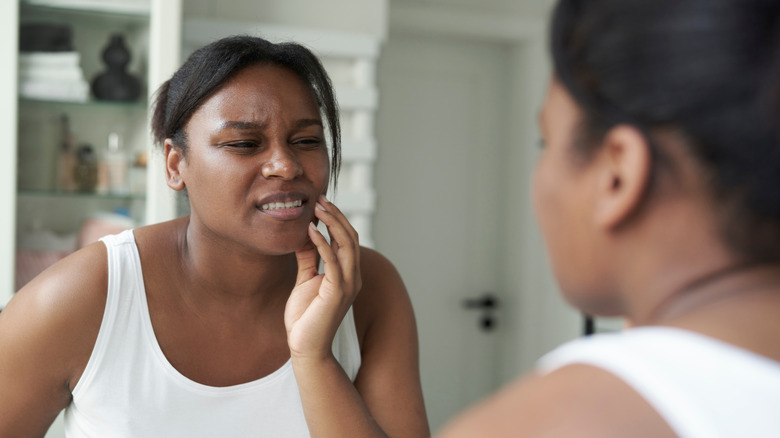A woman holding her jaw while looking in the mirror