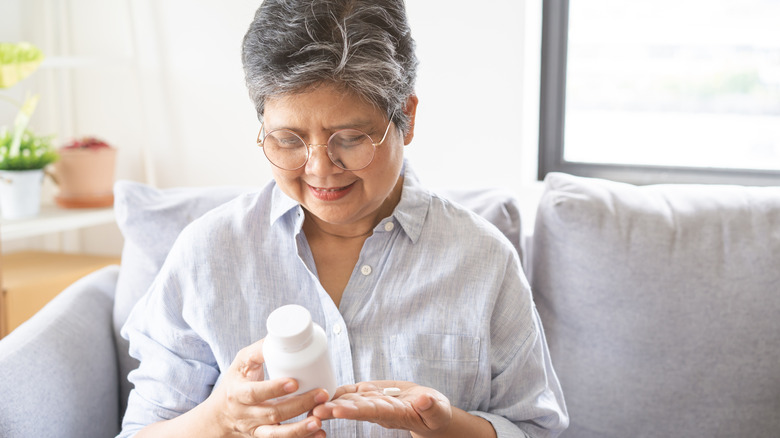 A woman holding a supplement pill while looking at the supplement bottle