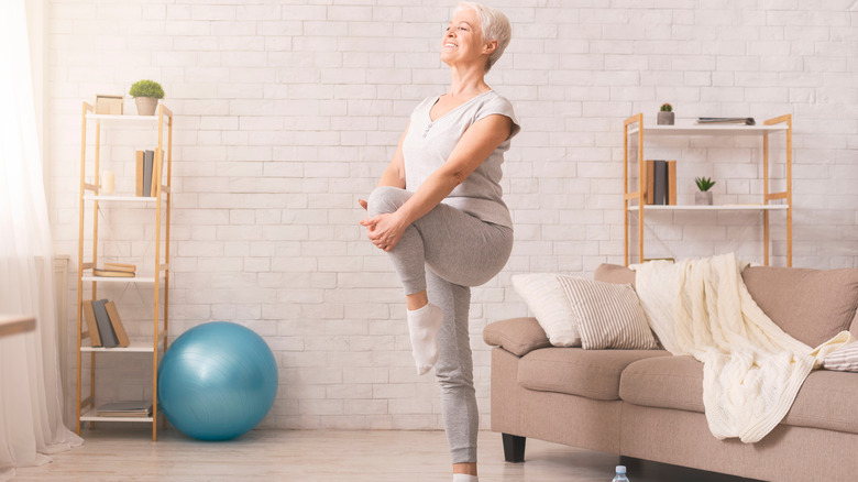 Woman standing up holding left knee with hands, stretching