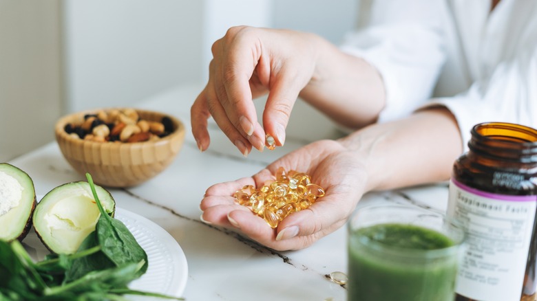 hands holding vitamin D capsules near food