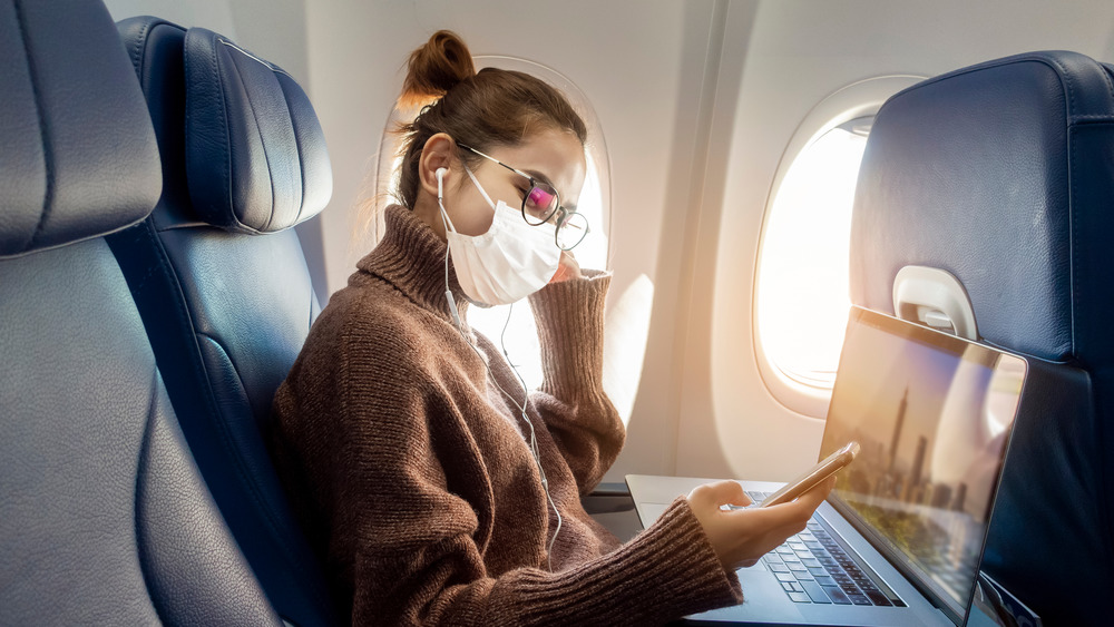 Young women seated on plane wearing face mask