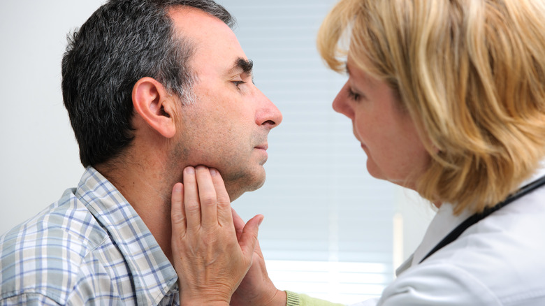 Female doctor touching a male patient's swollen throat