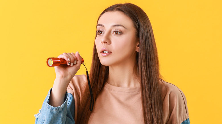 Woman on yellow background holding a red flashlight