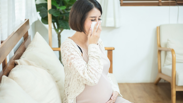Pregnant woman sneezing into tissue