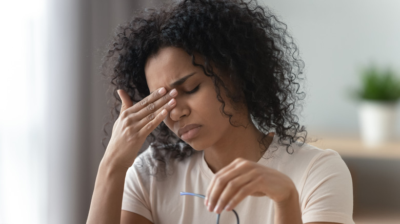 Woman holding forehead with glasses in her other hand