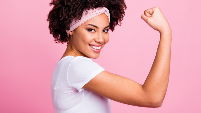 A smiling woman doing an arm curl to show off a toned tricep