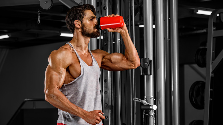 A sweaty, muscular man drinking a protein shake at the gym