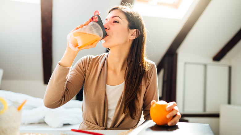 A woman drinks an orange drink at home